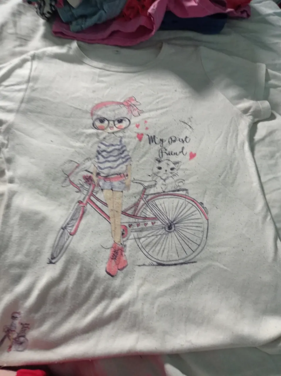 Remera blanca con estampa de nena en bicicleta y gatito.