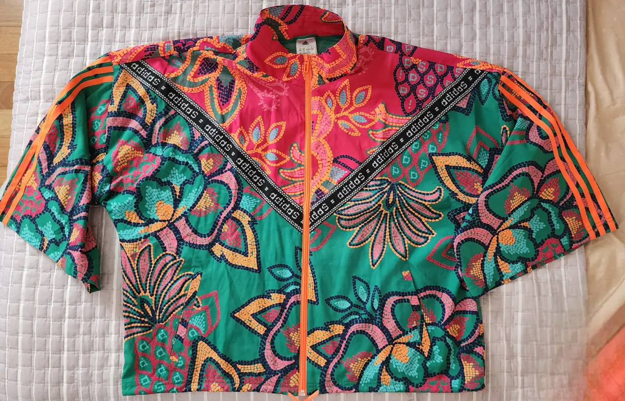 Campera deportiva Adidas con estampado floral vibrante. Diseño retro con cierre y detalles en naranja. Ideal para un look casual y con estilo.