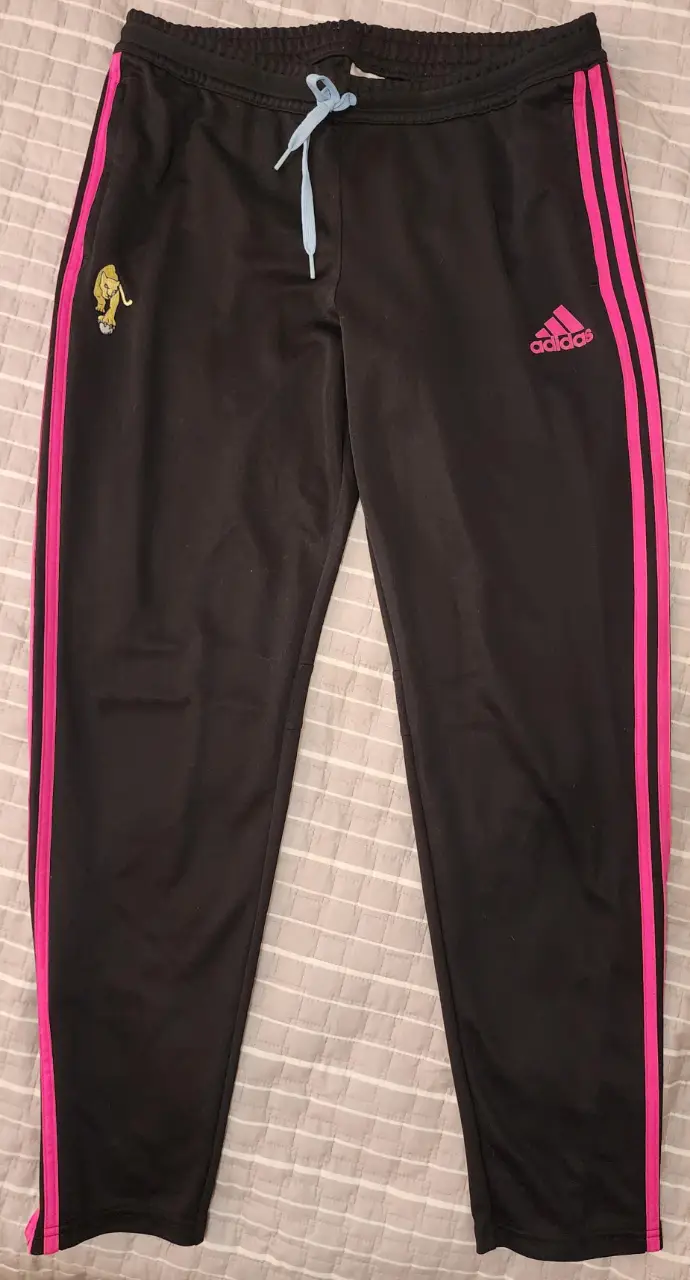 Pantalón deportivo Leonas Adidas negro con detalles en rosa. Tiene las tres tiras características de la marca en rosa a los costados y el logo de Adidas en rosa. Cuenta con un bordado de un león en la parte delantera. Talle XL.