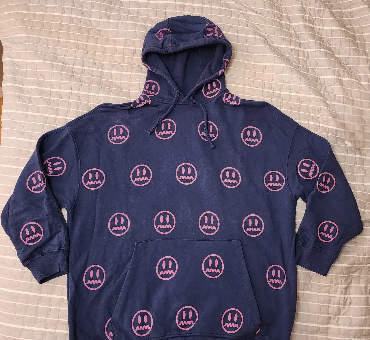 Buzo canguro azul marino con estampado repetido de caritas sonrientes rosas. Ideal para un look casual y cómodo.