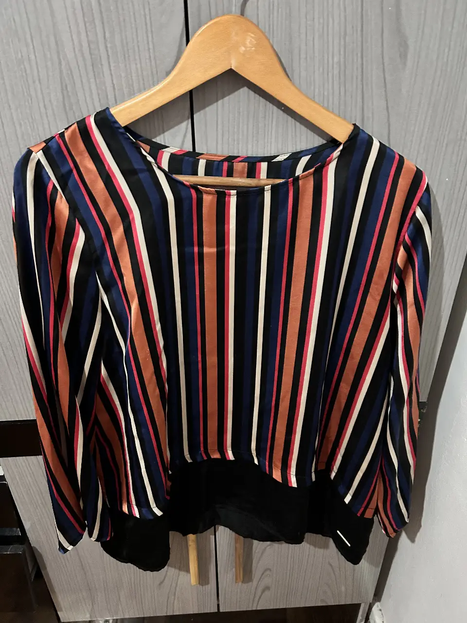 Blusa de mujer con estampado a rayas verticales en tonos naranja, azul, blanco y negro. Confeccionada en tela satinada, ideal para un look elegante y moderno. Talle L.