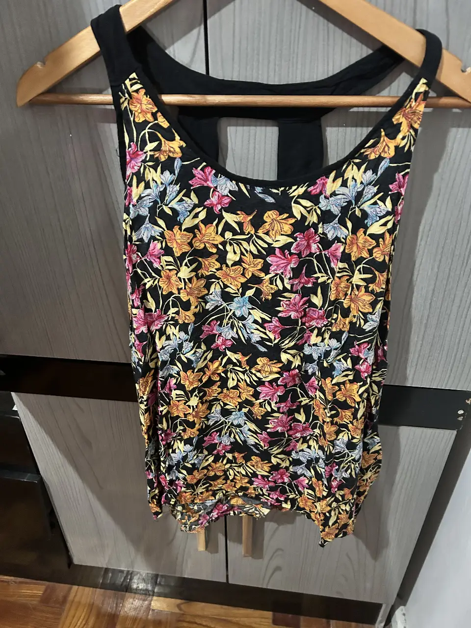 Musculosa de mujer con estampado floral en tonos amarillos, rosas y azules sobre fondo negro. Diseño con espalda deportiva y escote redondo. Ideal para un look fresco y casual.