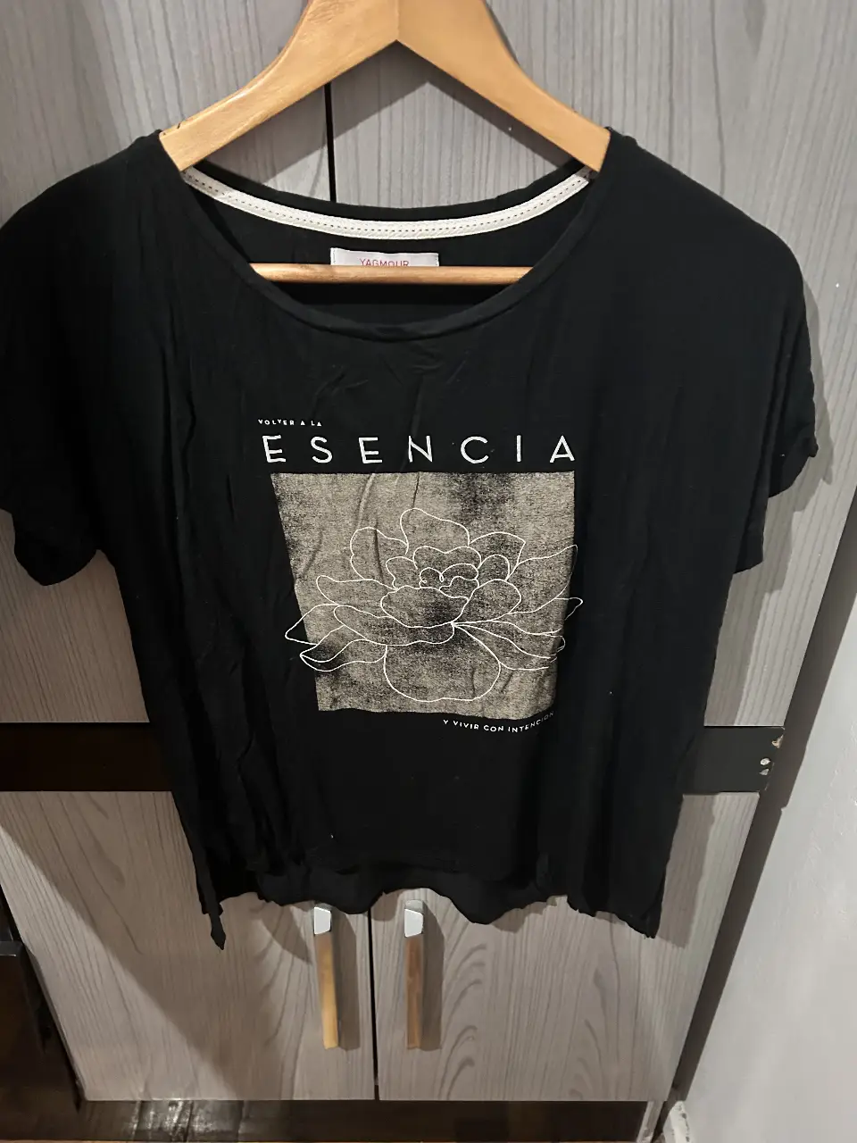 Remera negra de mujer de la marca Yagmour, con estampado de flor y frase "Volver a la esencia". Ideal para un look casual y cómodo.