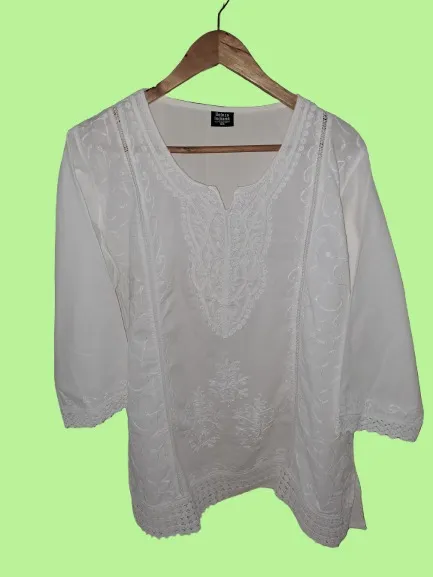 Blusa blanca de algodón con bordados florales y detalles de puntilla en mangas y ruedo. Diseño delicado y fresco, ideal para un look casual y elegante.