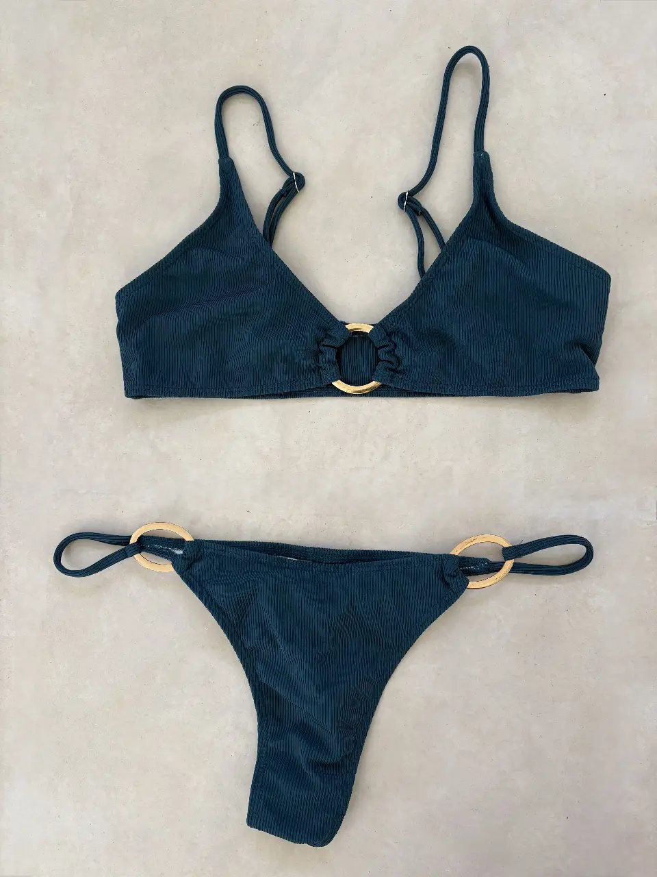 Conjunto de bikini verde oscuro con detalles dorados. Top con aro central y tirantes ajustables. Bombacha con detalles de aros dorados en los laterales.