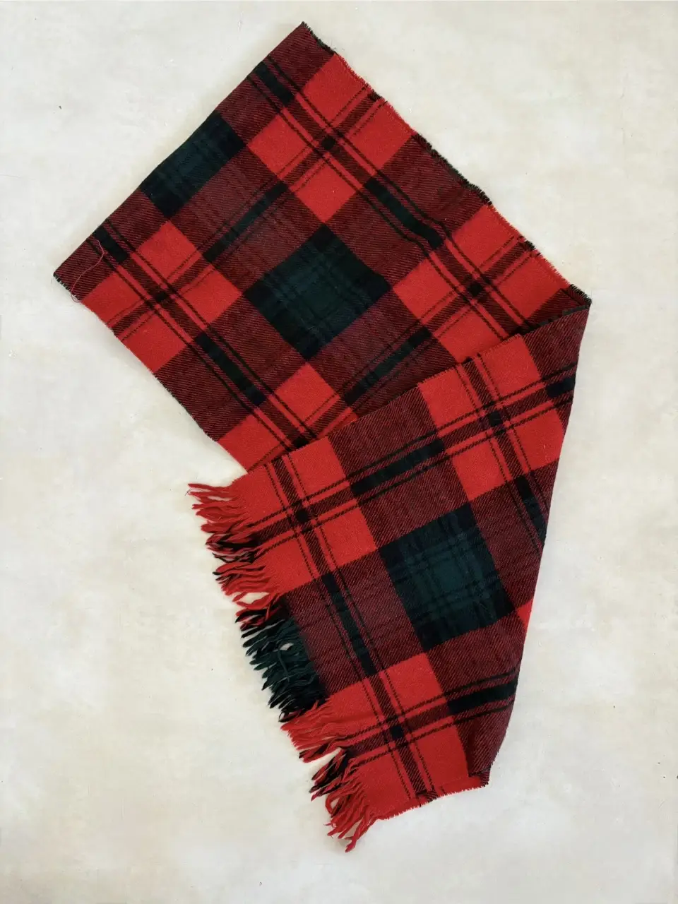 Bufanda escocesa a cuadros en rojo y negro. Ideal para el invierno, con flecos en los extremos. Un accesorio clásico y abrigado para cualquier look.