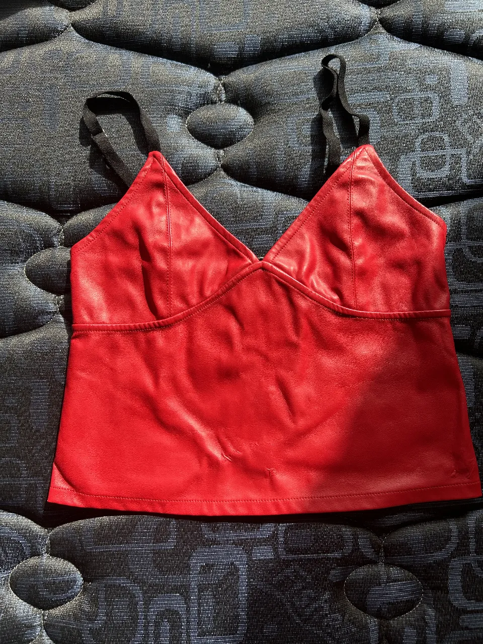 Top rojo de cuero sintético con tiras negras ajustables. Diseño con escote en V y cierre en la espalda. Ideal para un look de fiesta o salida.