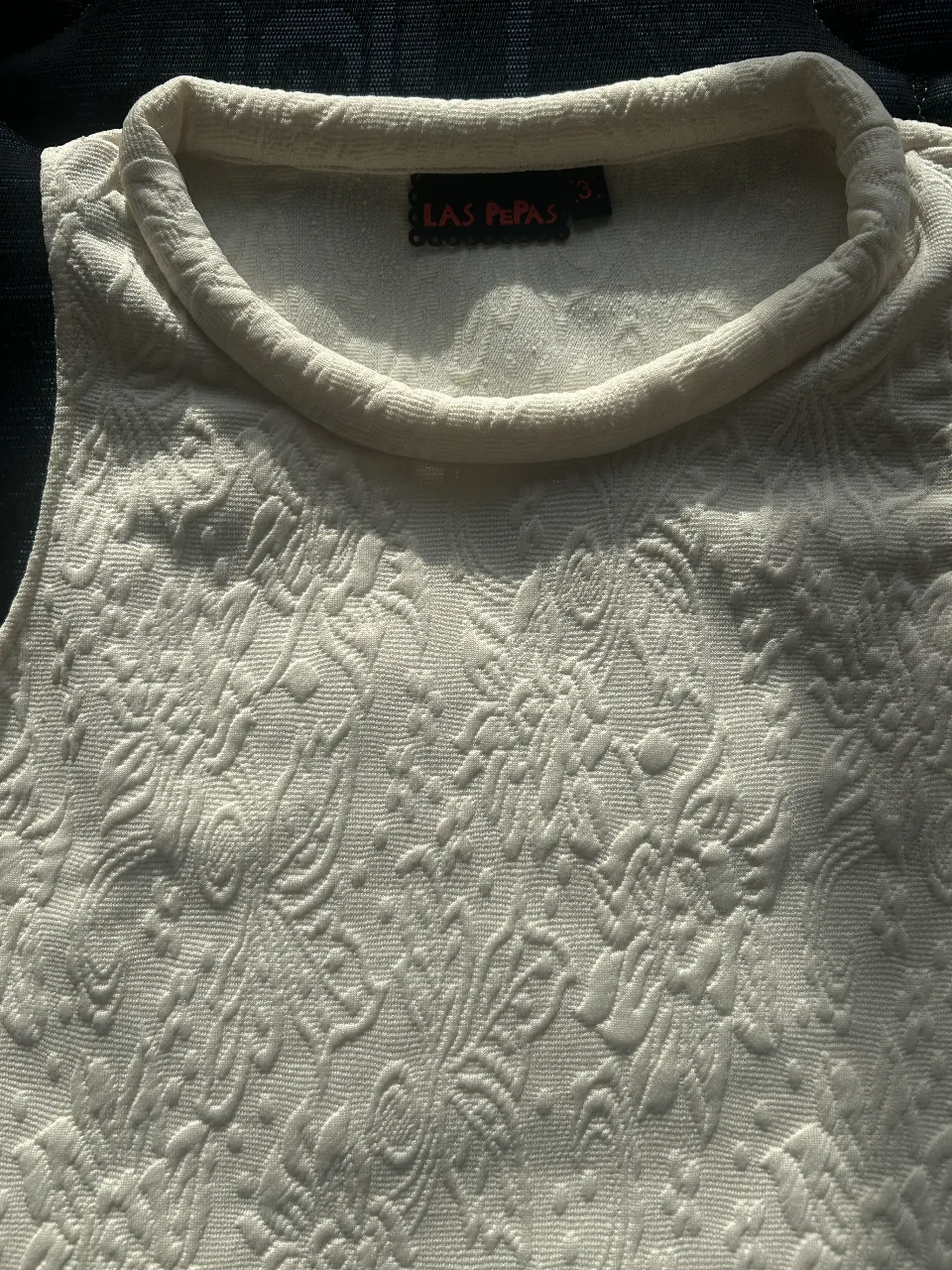 Top tejido de color crudo con diseño floral en relieve. Ideal para un look elegante y sofisticado.