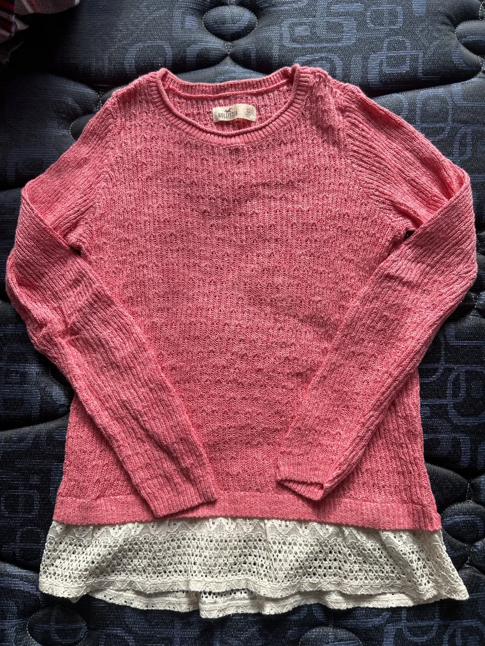Sweater rosa de tejido calado con detalle de encaje blanco en el bajo. Ideal para un look casual y femenino.