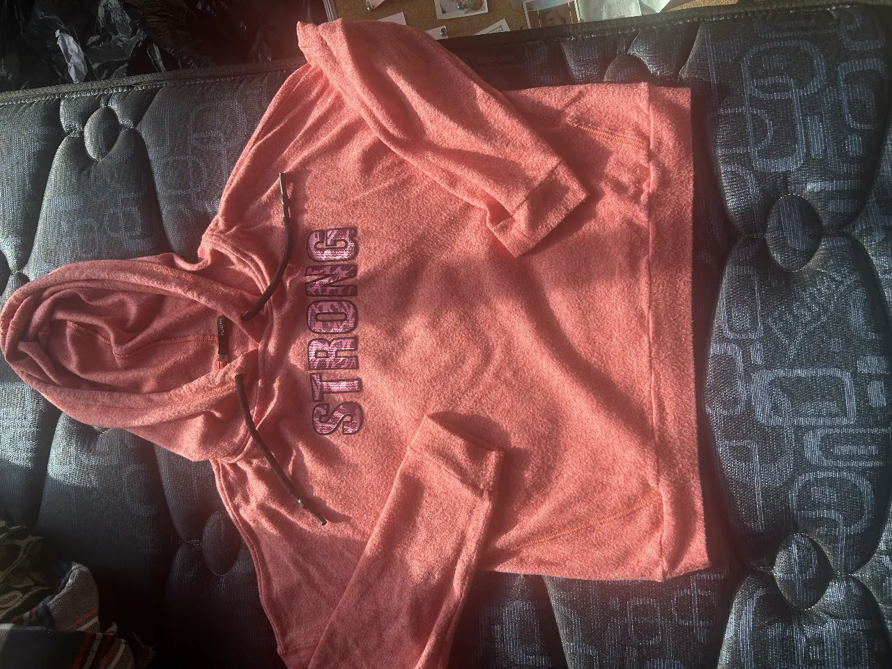 Buzo con capucha de color rosa, con la palabra 'STRONG' estampada en el frente. Ideal para un look casual y cómodo.