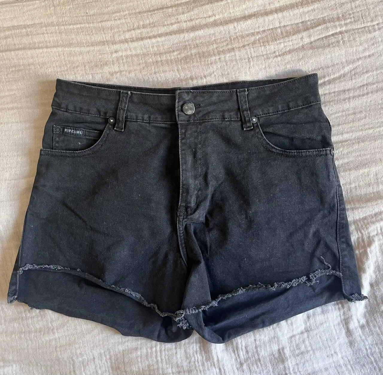 Shorts de jean negros (TALLE 28) con detalles deshilachados en el borde inferior. Tiro alto, ideales para un look casual y canchero.