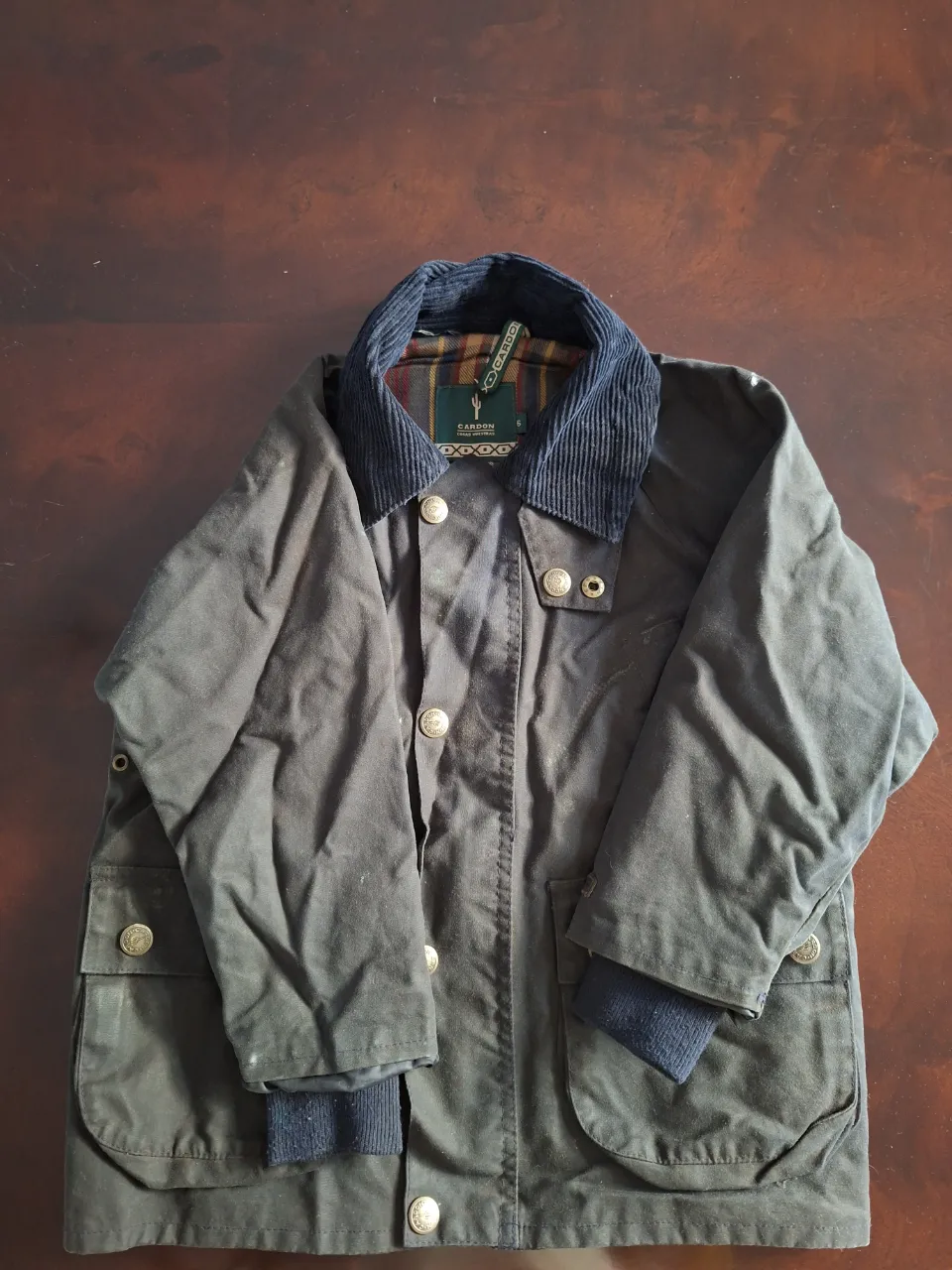 Campera de abrigo color verde oscuro con cuello de pana azul marino. Posee botones a la vista y bolsillos frontales con solapa. Puños de tejido acanalado.