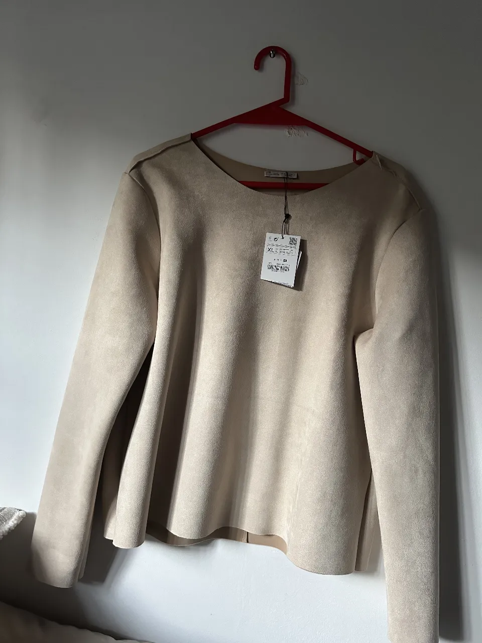 Blusa de gamuza sintética color crudo, manga larga y detalles en los hombros. Ideal para un look elegante y sofisticado.