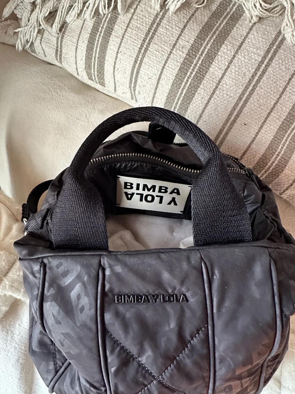 Bolso negro acolchado de la marca Bimba y Lola, con correa ajustable y detalles de la marca en relieve. Ideal para llevar tus esenciales con estilo y comodidad.