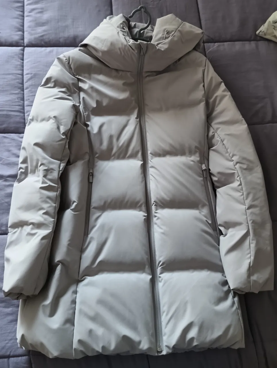 Camperón de pluma gris con capucha. Diseño acolchado y cierre frontal. Perfecta para un look casual y abrigado.