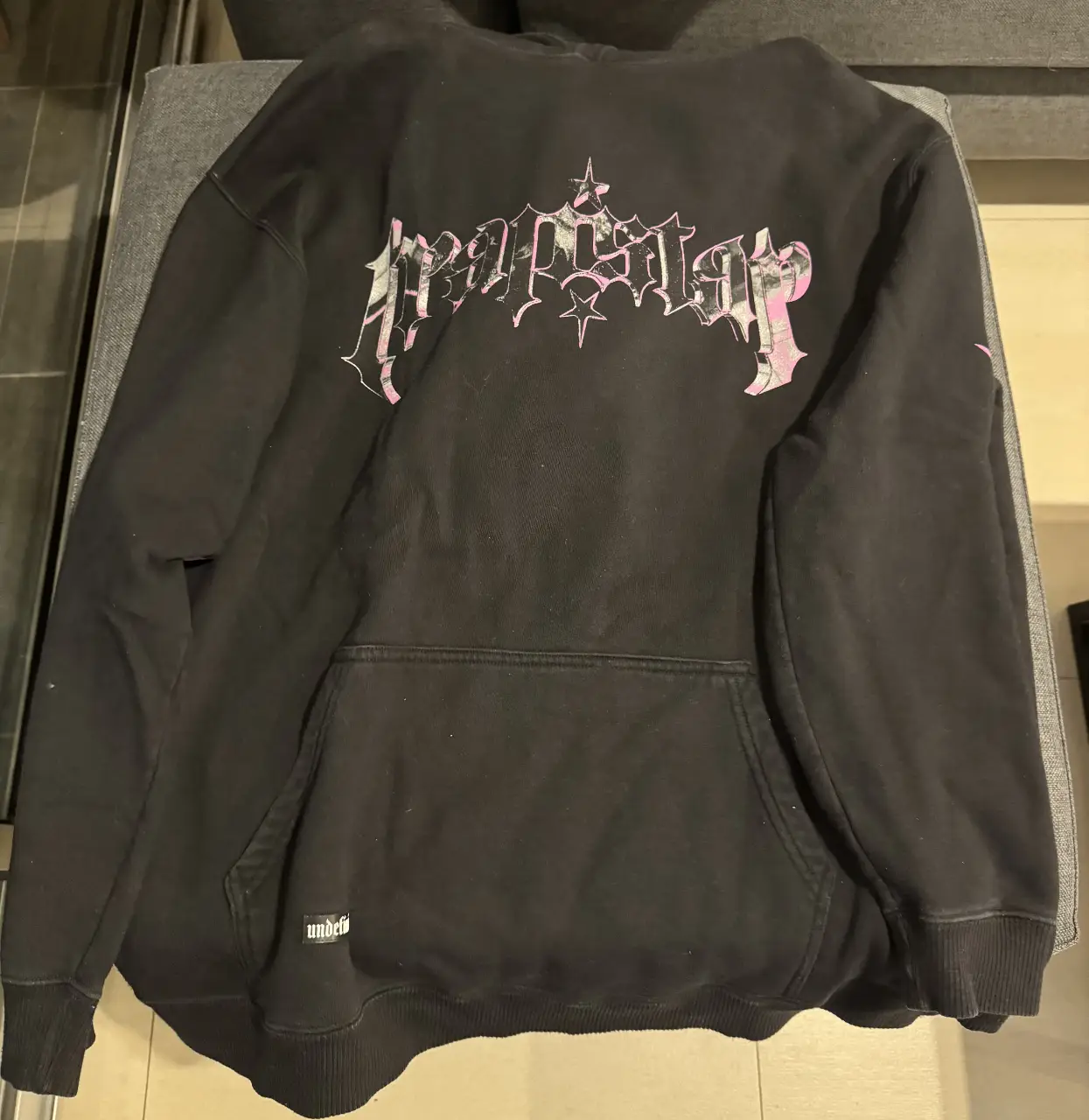 Buzo Undefined canguro negro con estampado "Trapstar" en la espalda y detalles en rosa. Diseño urbano y moderno, ideal para un look streetwear. Usado muy pocas veces.