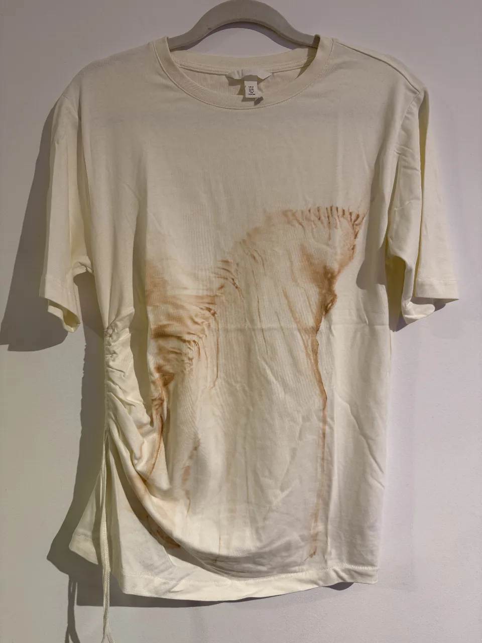 Remera de algodón color crema con diseño manchado en marrón. Tiene un detalle fruncido en un lateral.