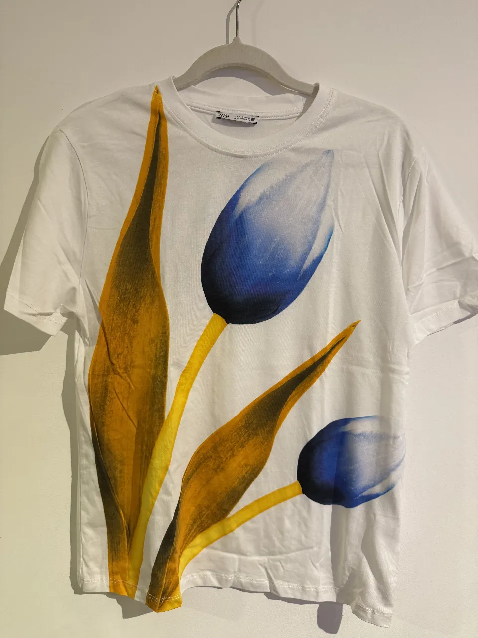 Remera blanca de algodón con estampado floral de tulipanes en tonos azules y amarillos. Ideal para un look casual y fresco.