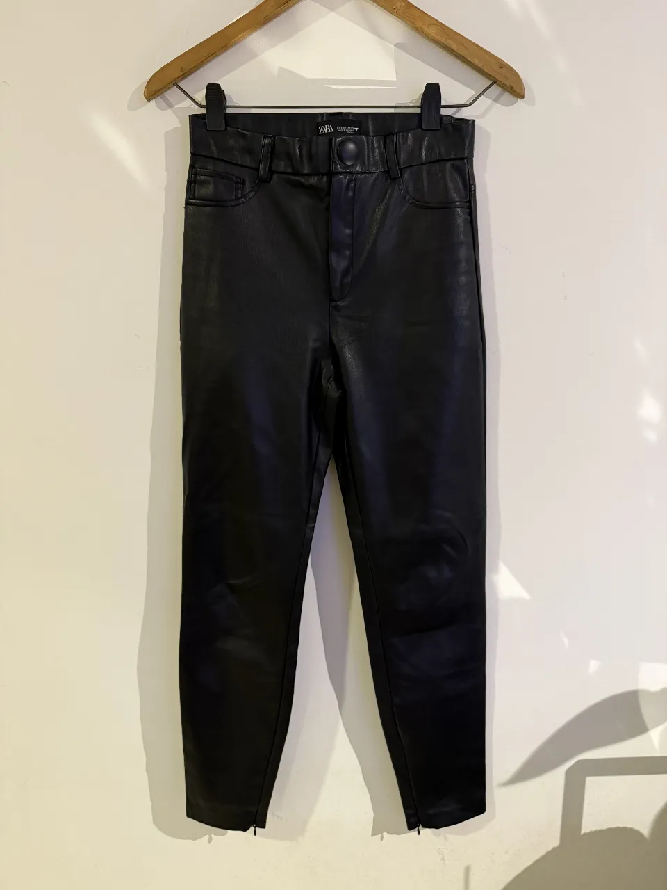 Pantalón sastrero de cuero sintético negro, tiro medio, con bolsillos delanteros y cierre en los tobillos. Ideal para un look moderno y sofisticado.