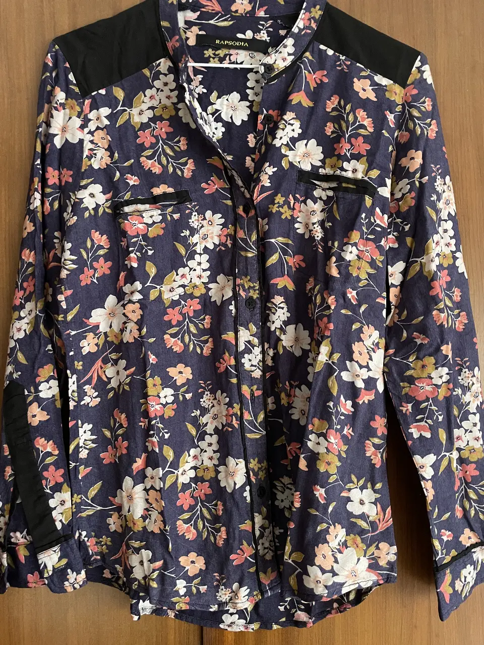 Camisa estampada de mujer, con flores en tonos azules, blancos y rosados. Cuello y detalles en negro. Marca Rapsodia.