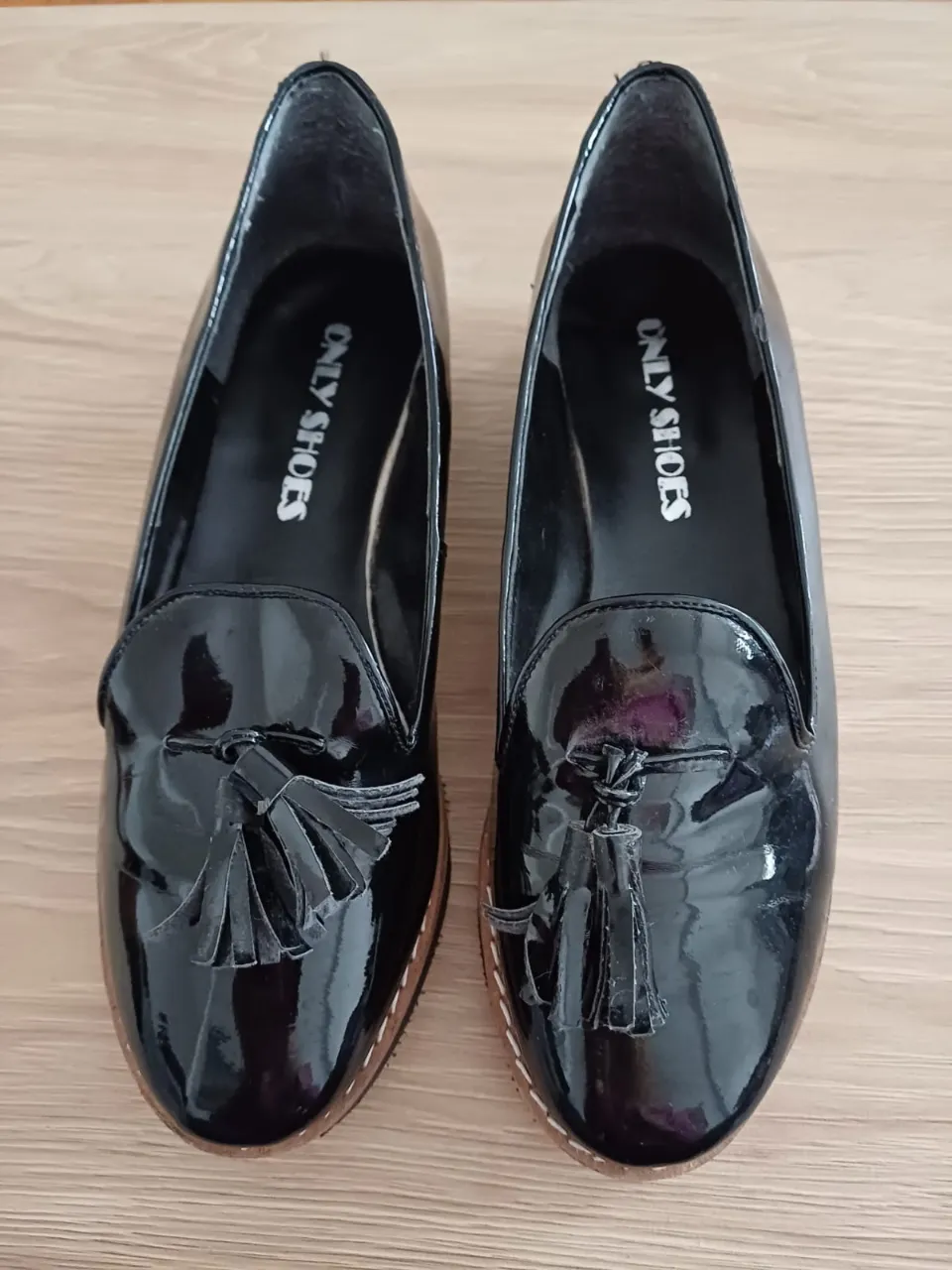 Mocasines de charol negro con detalle de borlas. Ideales para un look elegante y sofisticado.