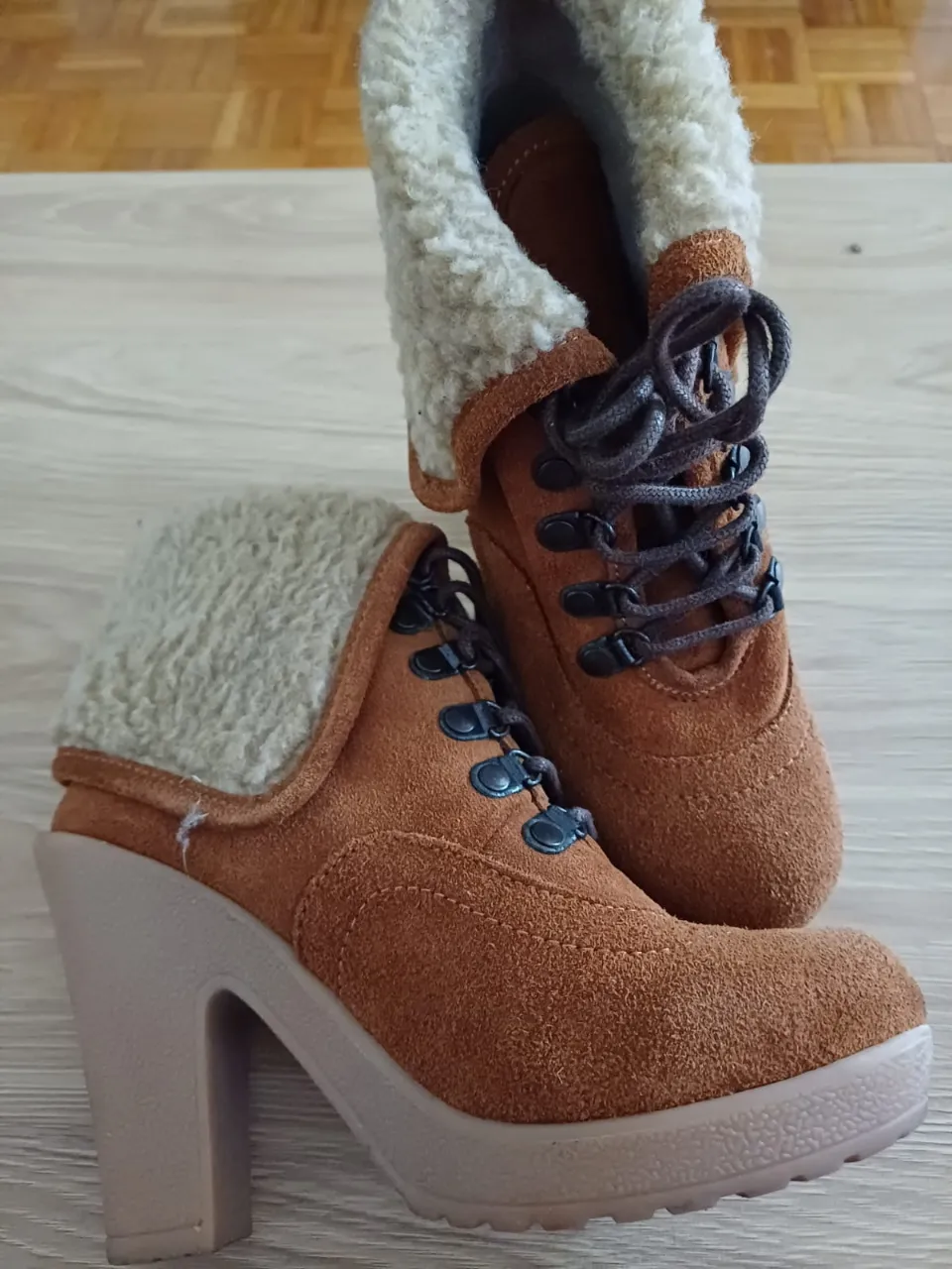 Botinetas de mujer con taco alto y detalle de peluche en el borde superior. Estilo acordonado con ojales metálicos y suela con relieve. Ideales para un look invernal y moderno.