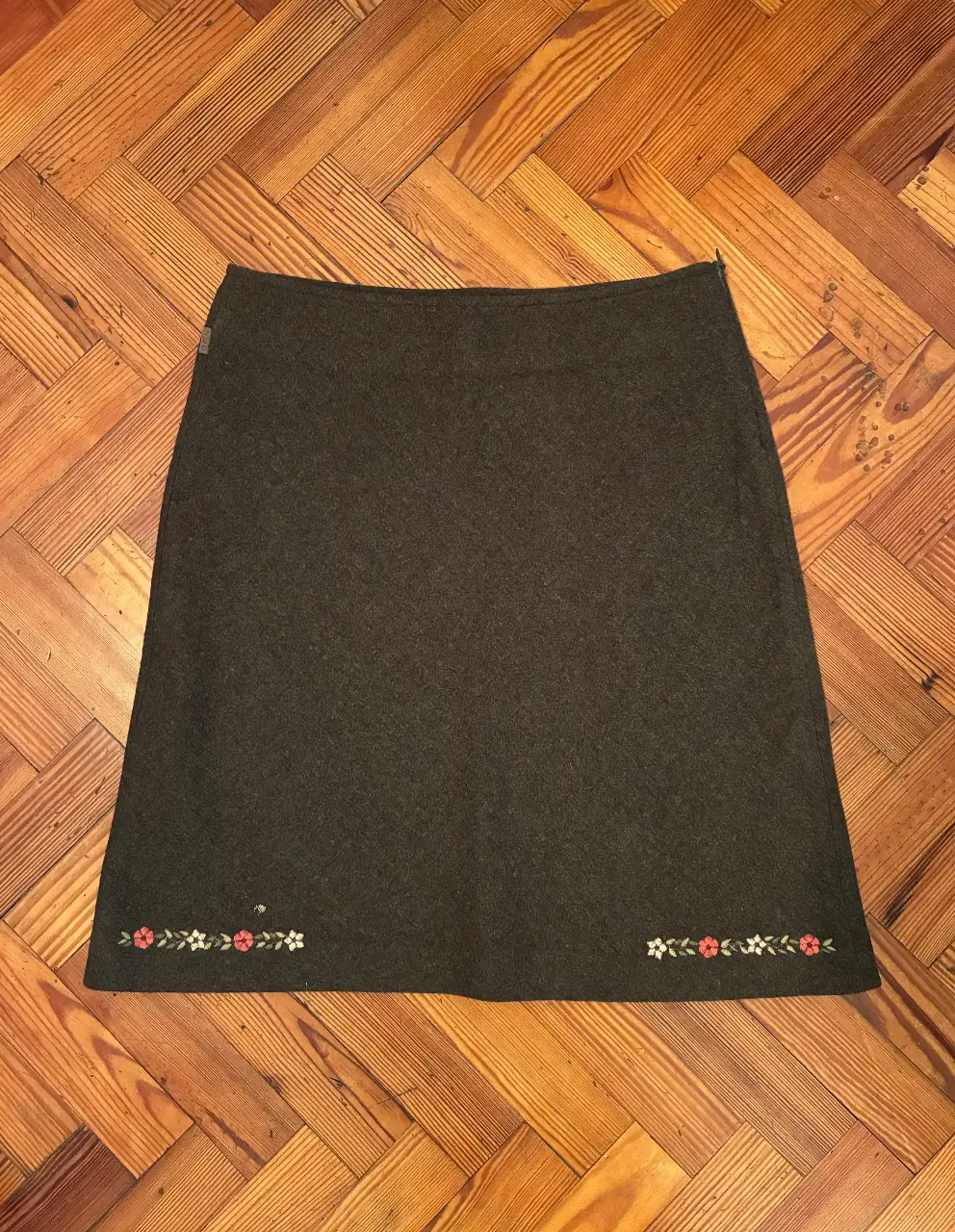 Pollera verde oscuro de corte recto con evade y detalle de bordado floral en el borde inferior. Ideal para un look elegante y versátil. 51cm de largo