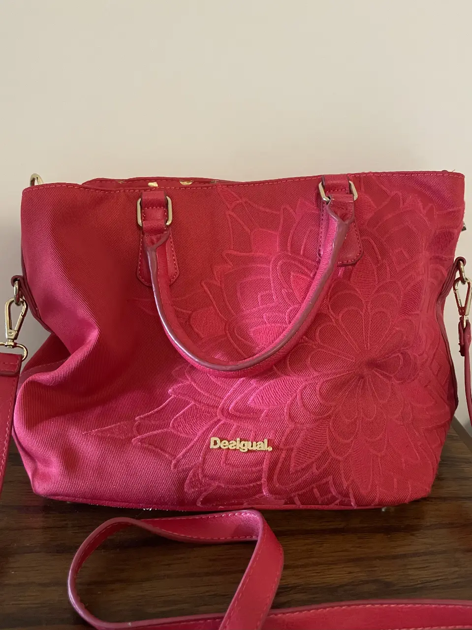 Cartera Desigual fucsia con diseño floral en relieve. Ideal para llevar al hombro o cruzada, con correa ajustable. Interior espacioso con múltiples compartimentos y detalles dorados. Perfecta para un look casual y con estilo. Usada y con detalles en la manija de atrás.