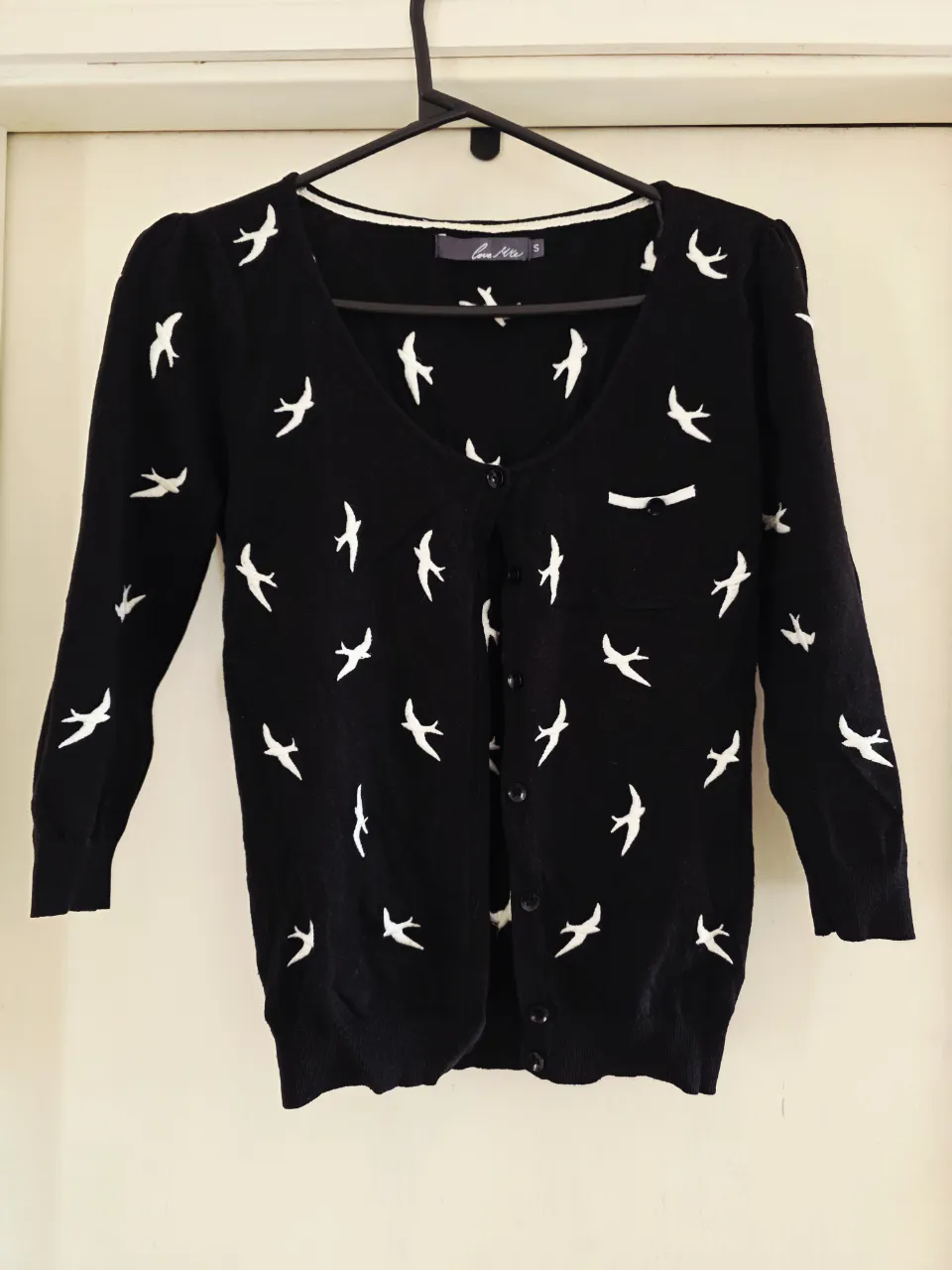 Cardigan negro con bordado de pajaritos blancos. Manga 3/4 y botones al frente. Detalle de bolsillo con solapa. Hermoso para combinar cualquier look. 
