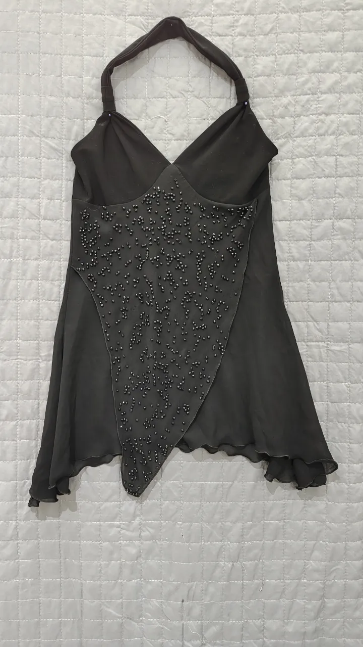 Top negro con breteles al cuello y detalles de pedrería en el frente. Diseño asimétrico y con caída, ideal para un look de noche o fiesta.