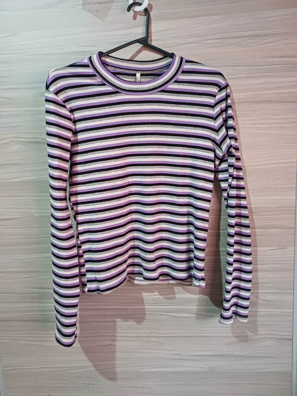 Remera de manga larga a rayas horizontales en blanco, negro, gris y violeta. Cuello redondo.