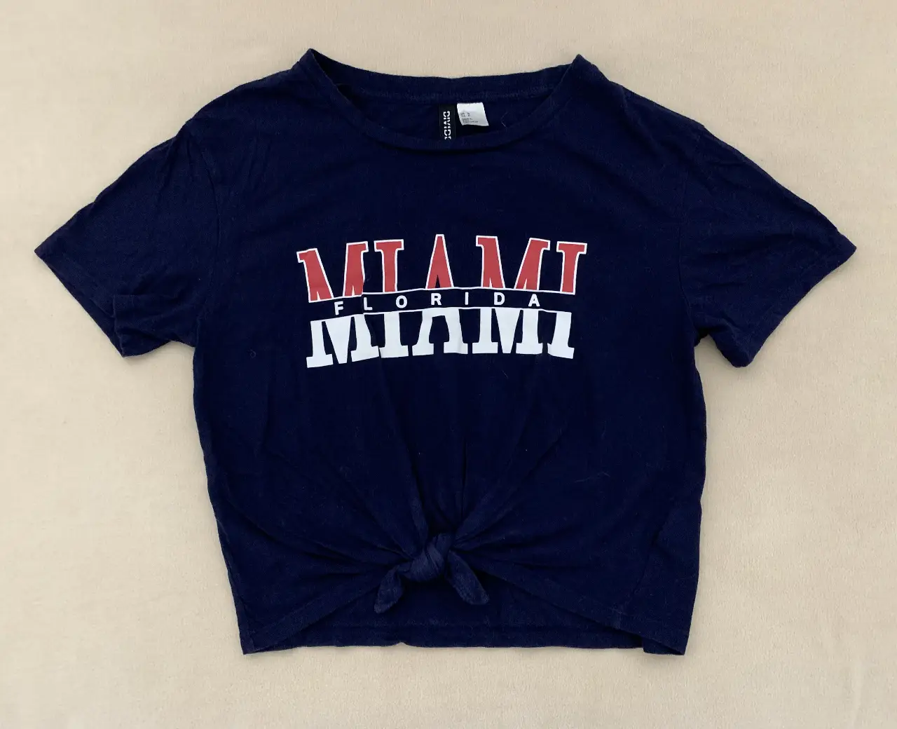 Remera de mujer H&M Divided, de color azul marino con estampado "Miami Florida" en blanco y rojo. Talle S. Ideal para un look casual y urbano.