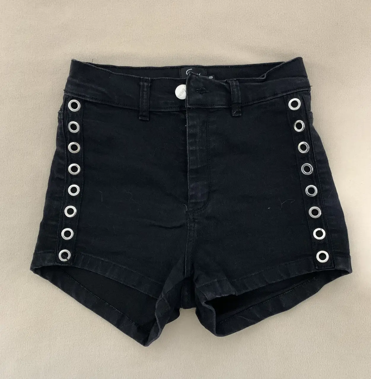 Short de jean negro con detalles de ojales plateados en los laterales. Tiro alto, ideal para un look moderno y canchero.