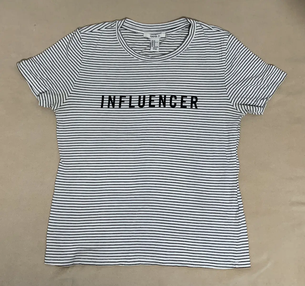 Remera de mujer a rayas horizontales blancas y negras, con la palabra "INFLUENCER" estampada en negro en el frente. Cuello redondo y mangas cortas. Ideal para un look casual y moderno.