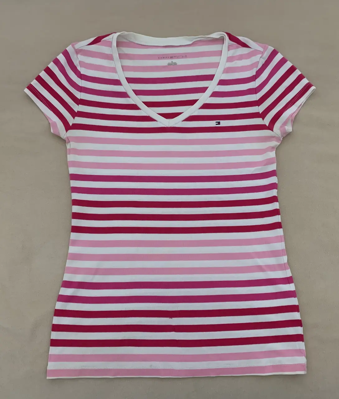 Remera Tommy Hilfiger a rayas horizontales en tonos rosa y blanco, con cuello en V y logo de la marca. Ideal para un look casual y fresco.