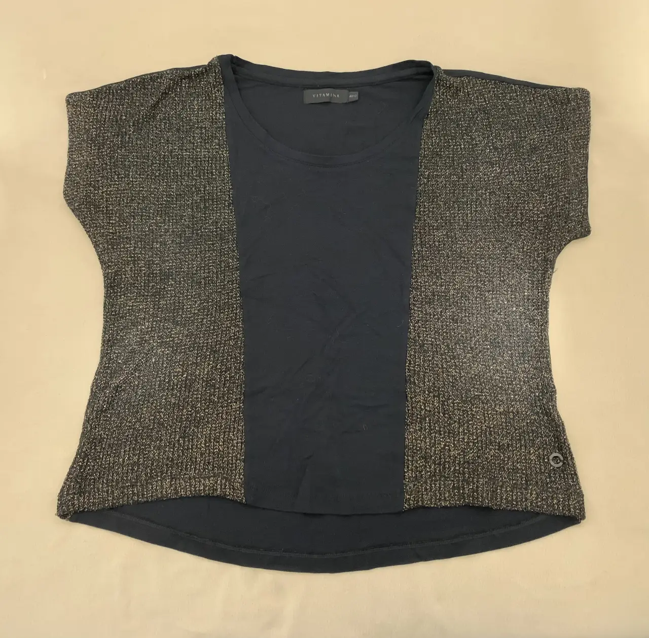 Remera de mujer con diseño bicolor. La parte central es de color negro liso, mientras que los laterales y mangas son de un tejido negro con brillo dorado. Cuello redondo y corte recto. Marca Vitamina. Talle 40.