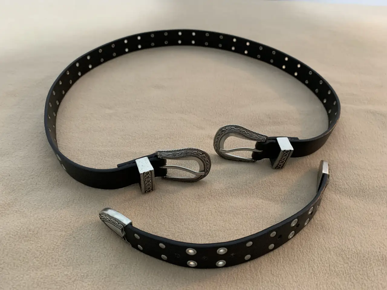 Cinturón de cuero negro con detalles plateados. Hebilla y puntera con diseño. Ideal para darle un toque rockero a tu look.