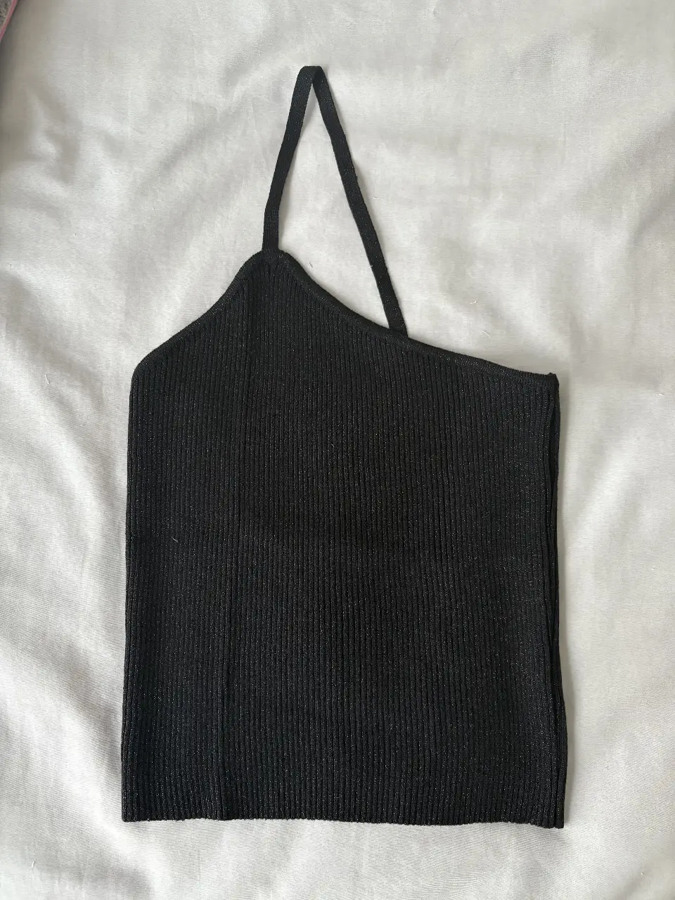 Top negro asimétrico de tejido de punto, con un solo tirante. Ideal para un look moderno y versátil. Negro con sutiles brillitos
