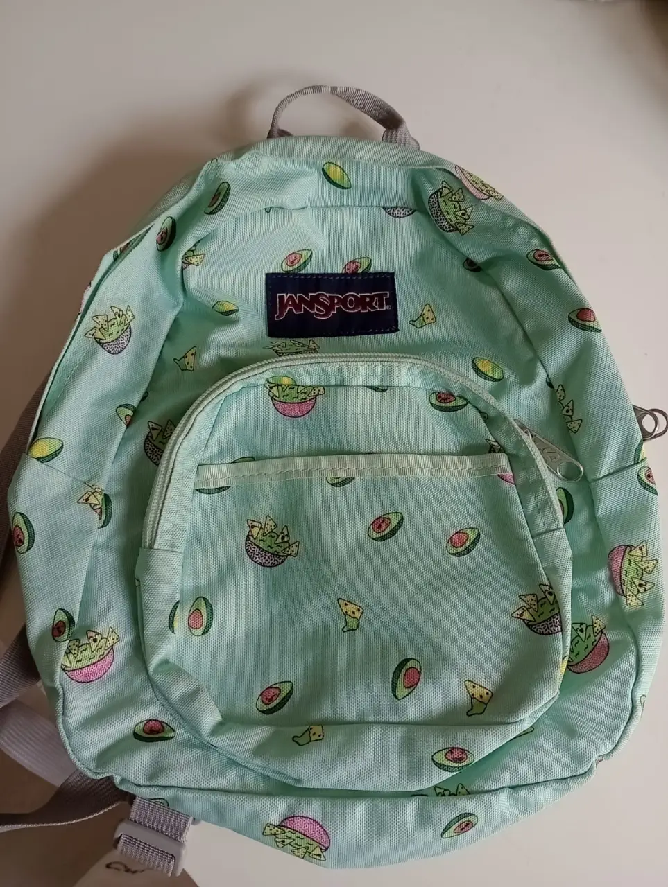 Mochila JanSport con estampado de aguacates y nachos. Ideal para uso diario o para llevar a la escuela. Cuenta con un bolsillo frontal con cierre y correas ajustables.