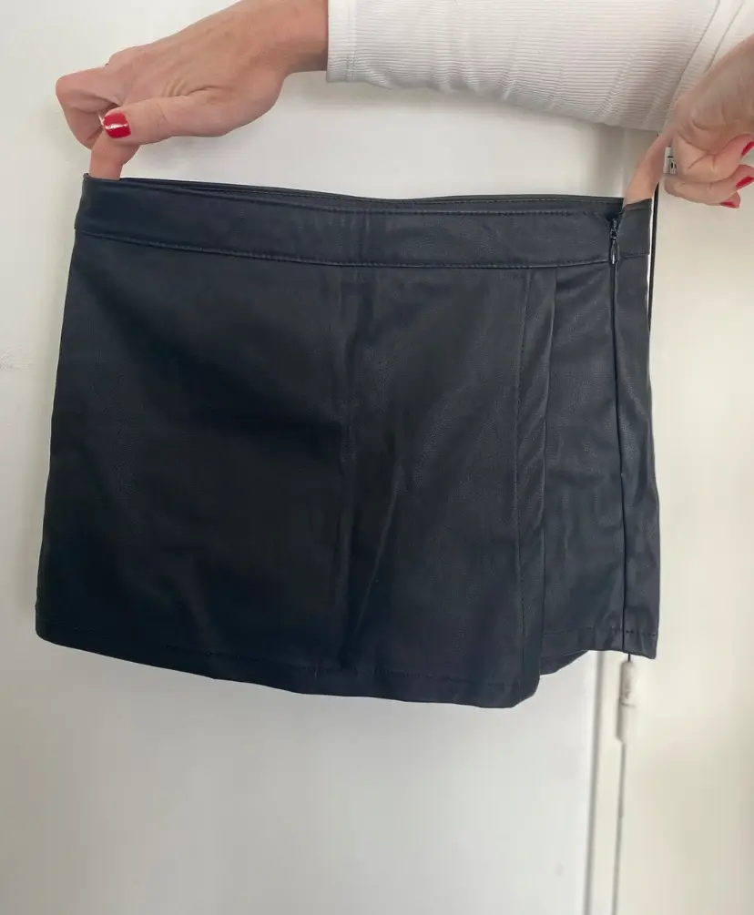 Minifalda de cuero sintético negra, con detalle de solapa cruzada y cierre lateral. Ideal para un look moderno y audaz.