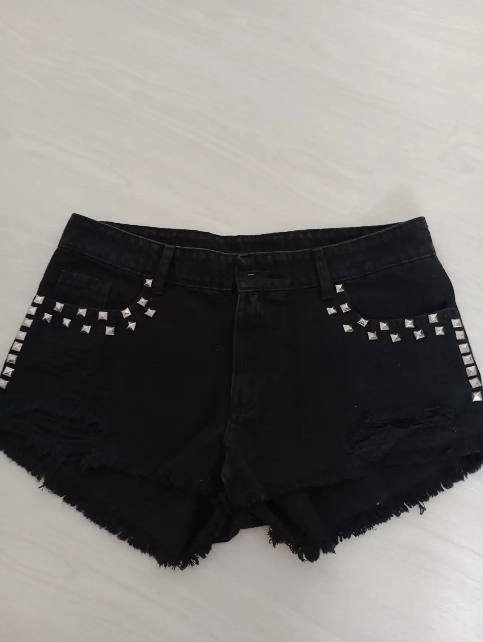Short de jean negro con detalles de tachas plateadas. Corte desflecado y tiro medio. Ideal para un look rockero y canchero.