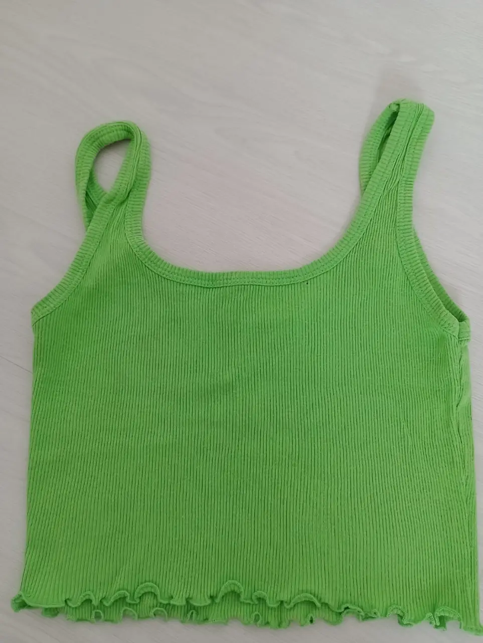 Top musculosa de color verde, con detalle de volados en la parte inferior. Ideal para un look casual y fresco.