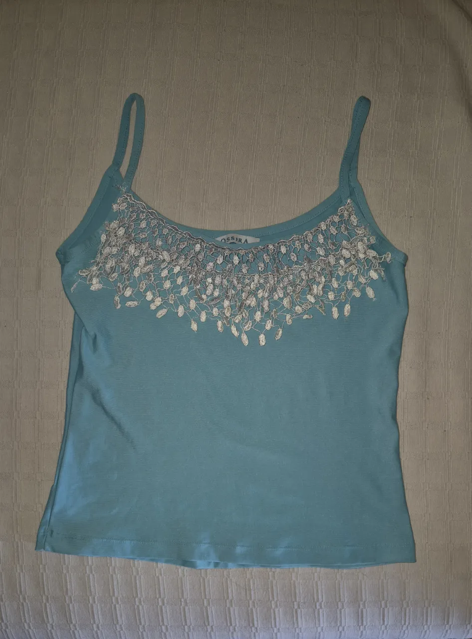 Musculosa color turquesa, con detalles de encaje y mostacillas en el escote. Ideal para un look casual y fresco.