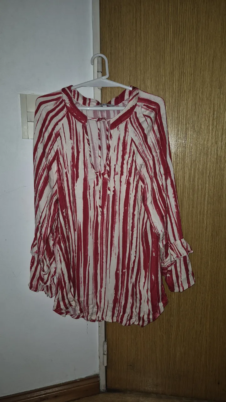 Blusa manga larga con estampa de rayas verticales en rojo y blanco. Posee cuello con tajo y lazo, y mangas con volados. Ideal para un look casual y canchero.