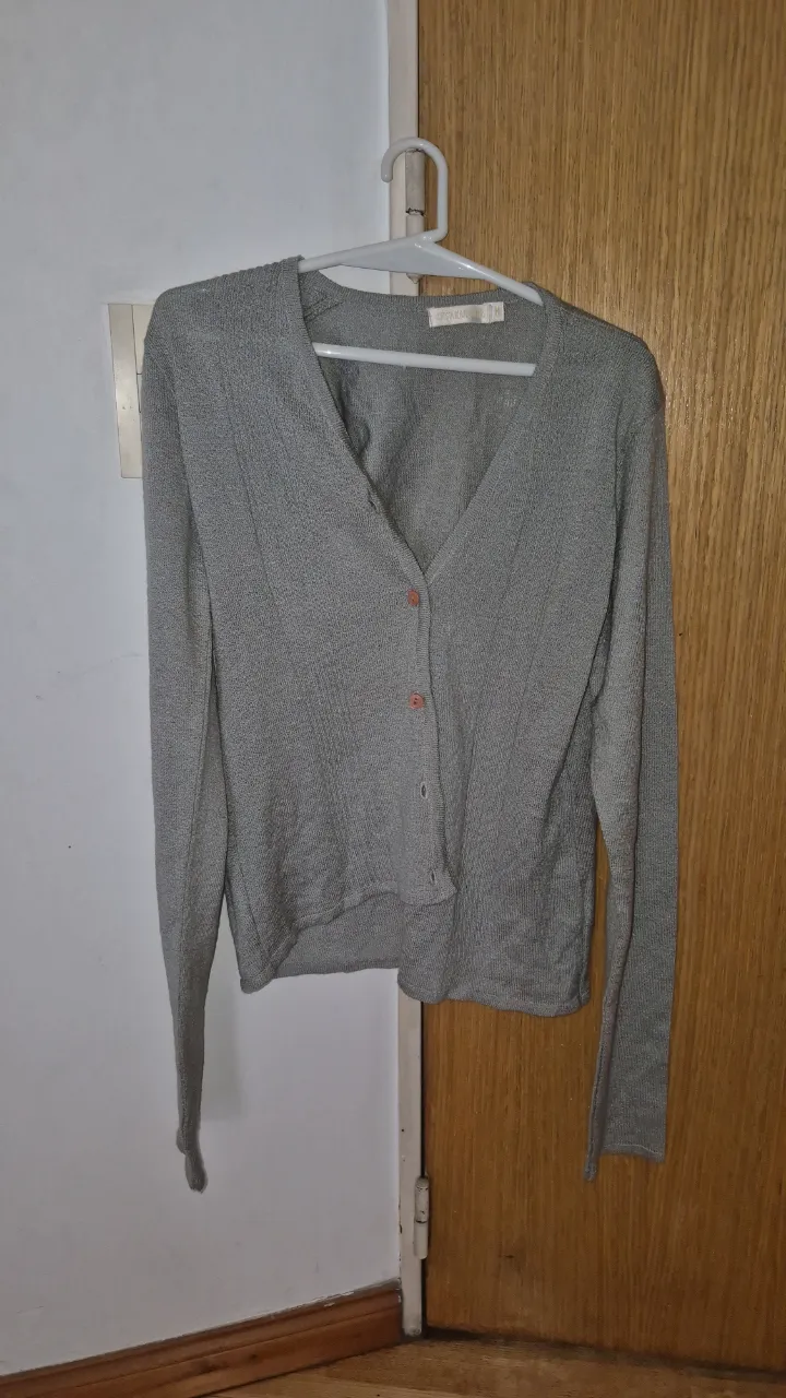 Cardigan gris de tejido liviano, con botones al frente y escote en V. Ideal para un look casual y cómodo.