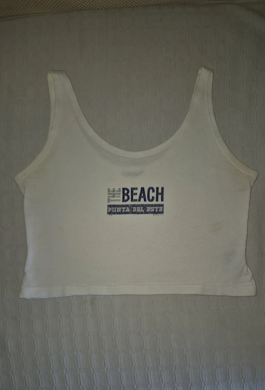 Musculosa blanca corta con estampa "BEACH PUNTA DEL ESTE" en azul. Ideal para un look playero y casual.