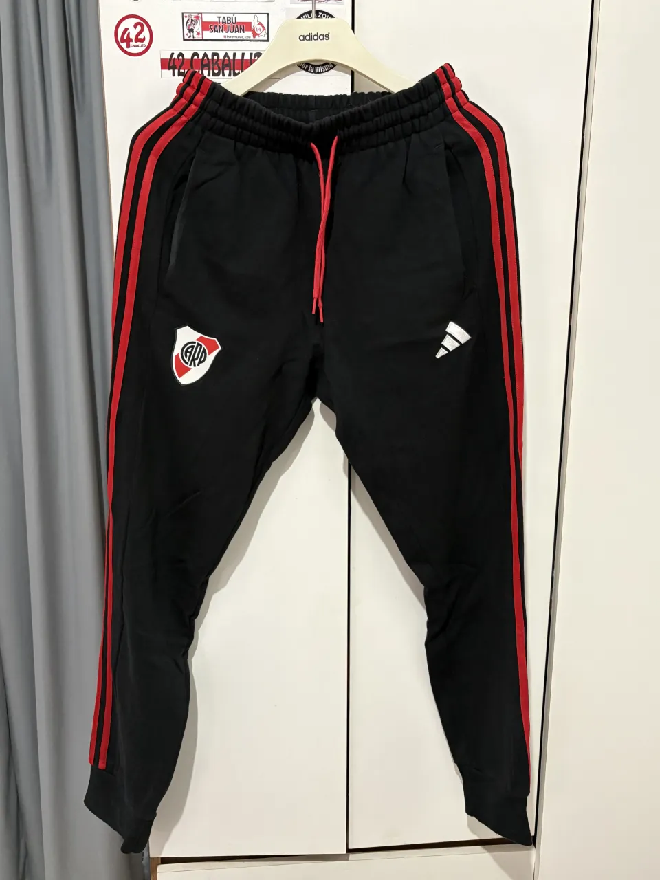Pantalon de River Plate, negro con franjas rojas en los laterales. Ideal para los fanáticos del club. Cómodo y canchero para el día a día.