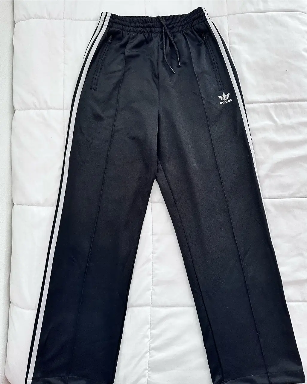 Pantalón deportivo Adidas negro con las tres tiras blancas a los costados. Tiro medio, con cintura elastizada y cordón para ajustar. Bolsillos laterales con cierre. Ideal para un look casual y cómodo. ORIGINAL ADIDAS