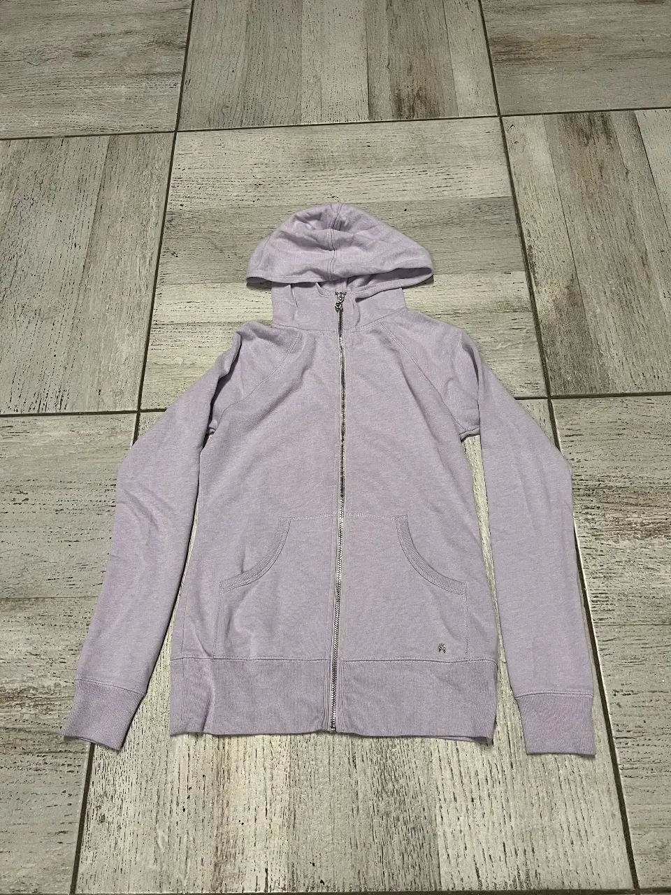 Buzo con cierre y capucha de color lila, con detalle de alas doradas en la espalda. Ideal para un look casual y cómodo.