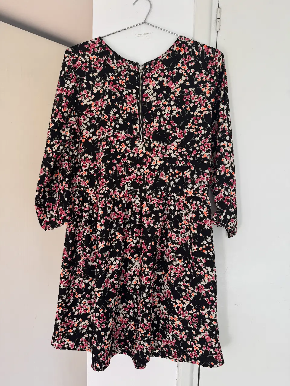 Vestido midi negro con estampado floral en tonos rosa y blanco. Diseño con cierre en la parte delantera y mangas 3/4. Ideal para un look casual y femenino.